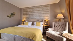 A hotel room with a large bed, a tufted headboard, a grey armchair, and a small wooden side table. - Hotel Zum Leineweber (Burg (Spreewald))