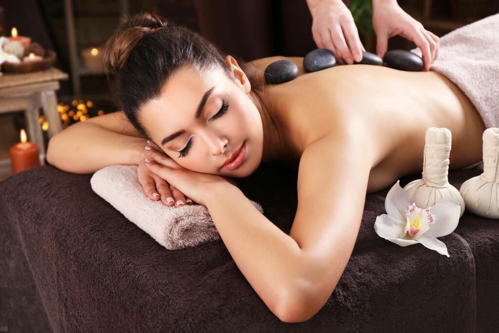 A person receiving a massage with stones on their back, a towel, and a flower on the side.