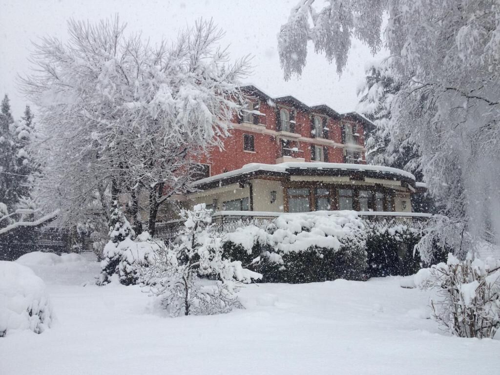 A building with a snow-covered roof and surrounding trees, indicating a winter setting.