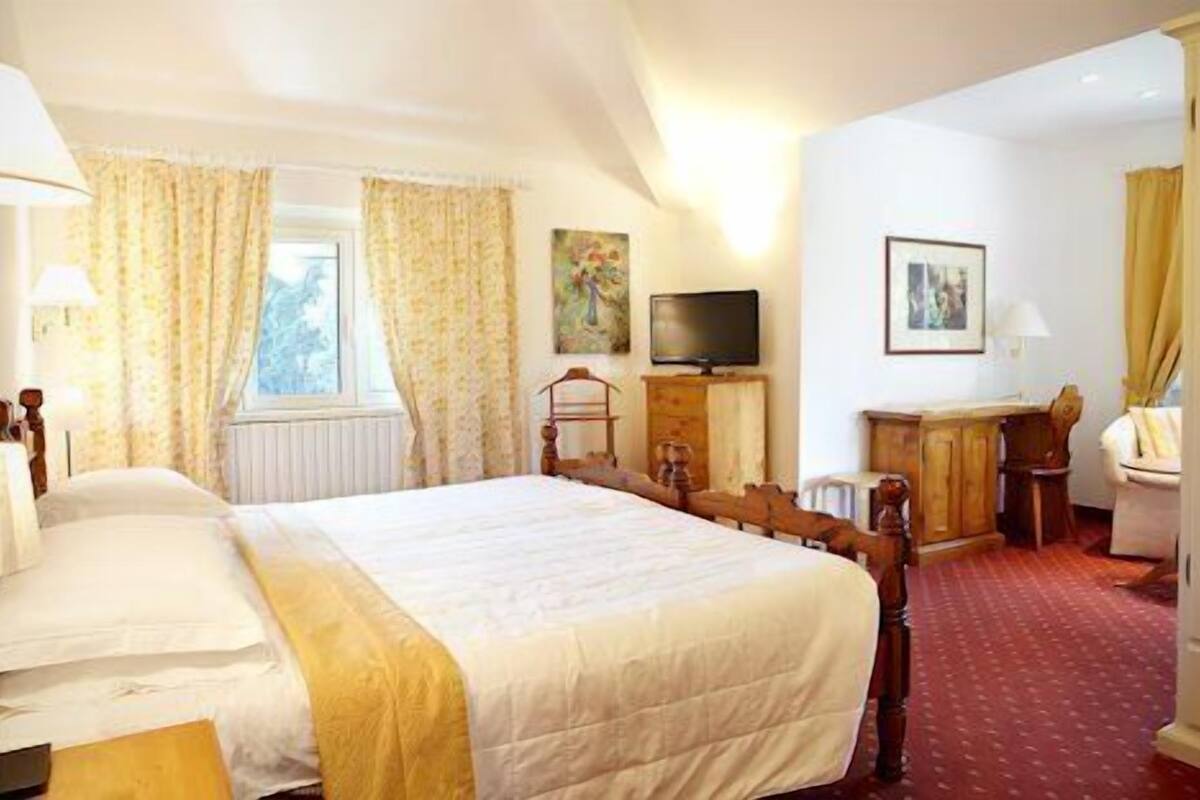 A hotel room with a large bed, a desk, a chair, a television, and a window with curtains.
