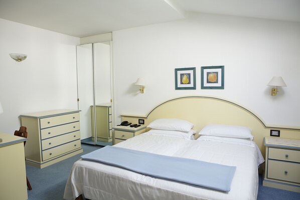 Habitación de hotel con cama, mesitas de noche, cómoda, espejo y dos cuadros en la pared.