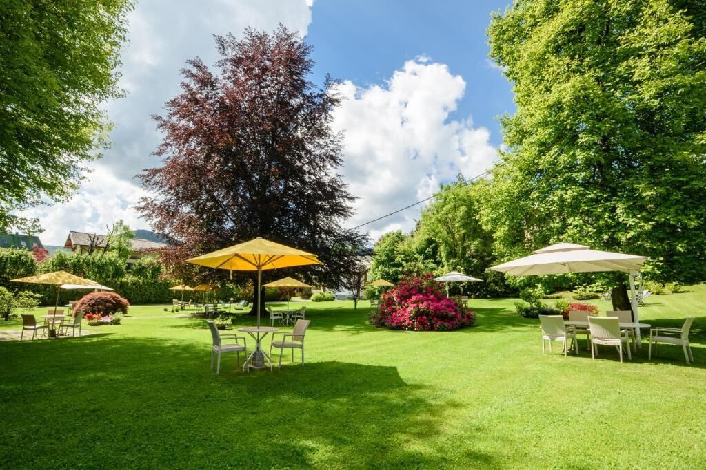 An outdoor patio area with tables and chairs under umbrellas, surrounded by lush greenery and trees.