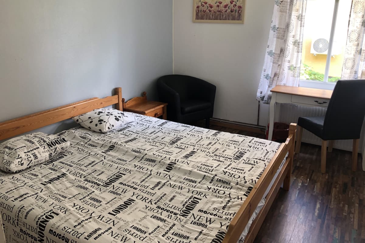 A bedroom with a bed, a desk, a chair, and a window with curtains.