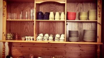 A wooden cabinet with shelves containing glassware, cups, bowls, and plates.