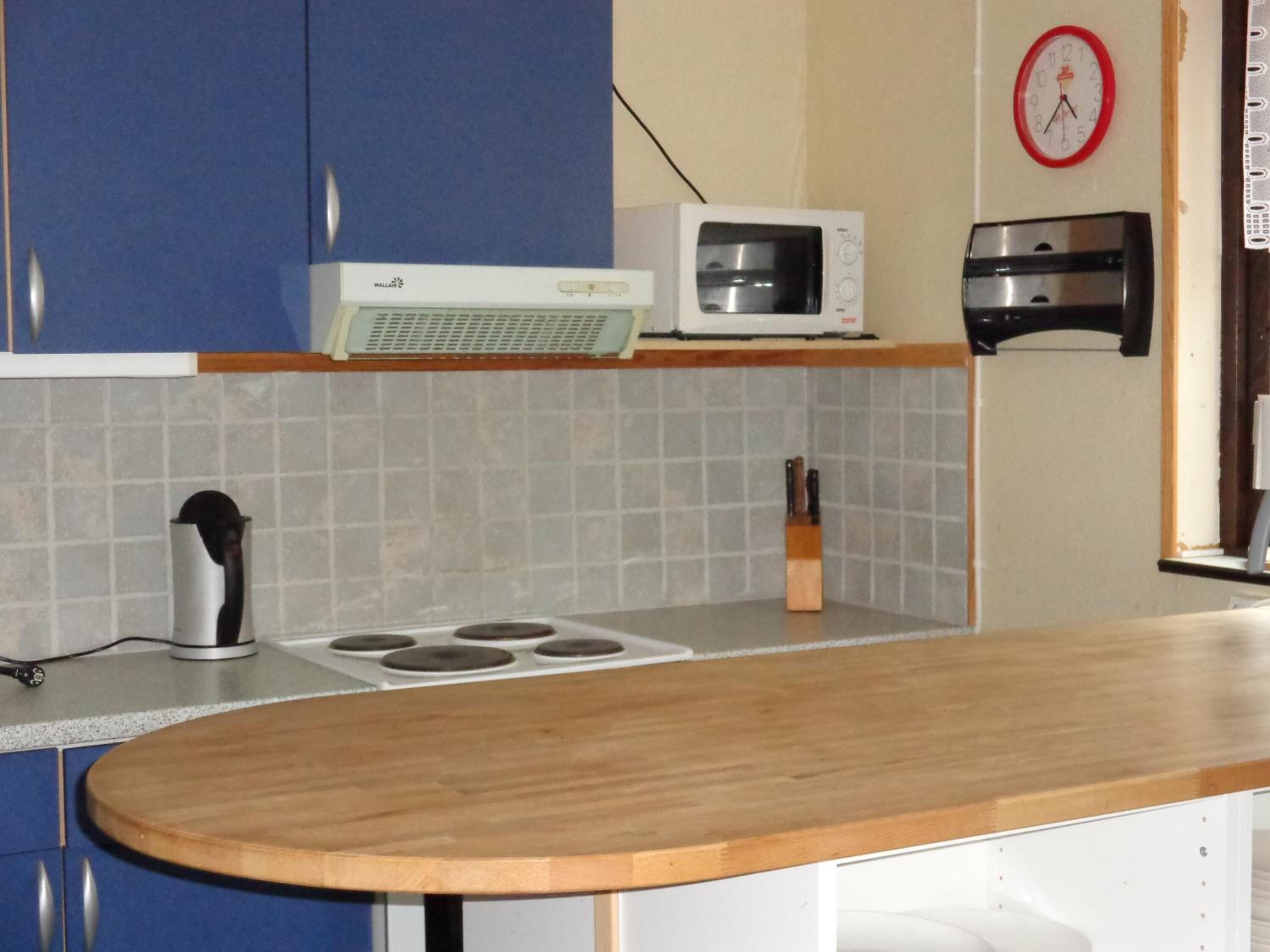 A kitchen with blue cabinets, a microwave, a toaster, and a clock on the wall.
