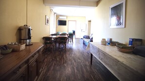 Un comedor con mesa y sillas de madera, una cafetera y un televisor en la pared.