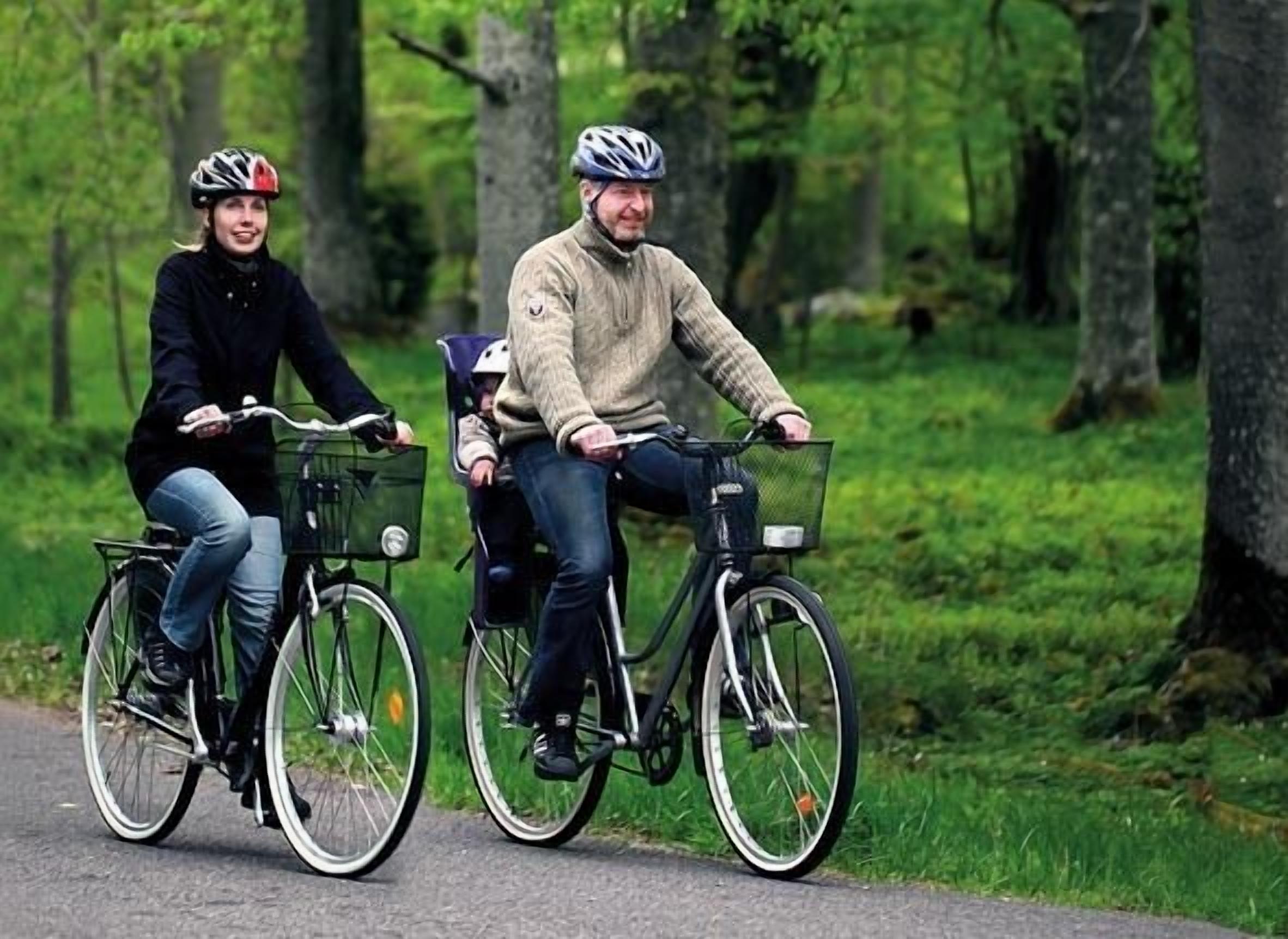 Two people riding bicycles on a paved path in a wooded area.