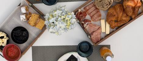 Une table dressée pour le petit-déjeuner, avec du pain, des viennoiseries, de la charcuterie, du fromage et diverses garnitures.