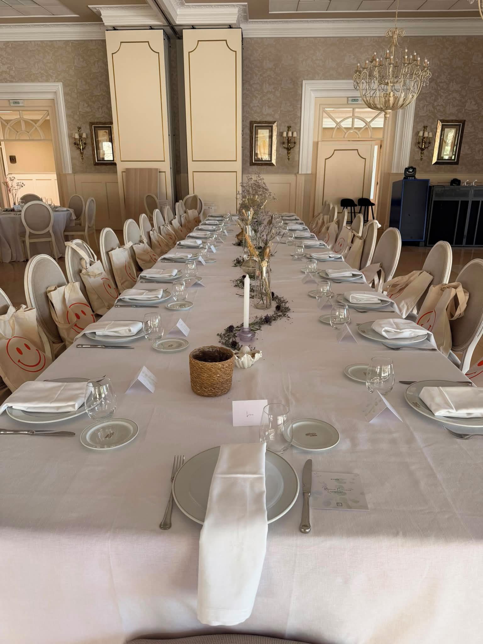 A long banquet table set for a formal event with chairs, plates, glasses, and a central floral arrangement.