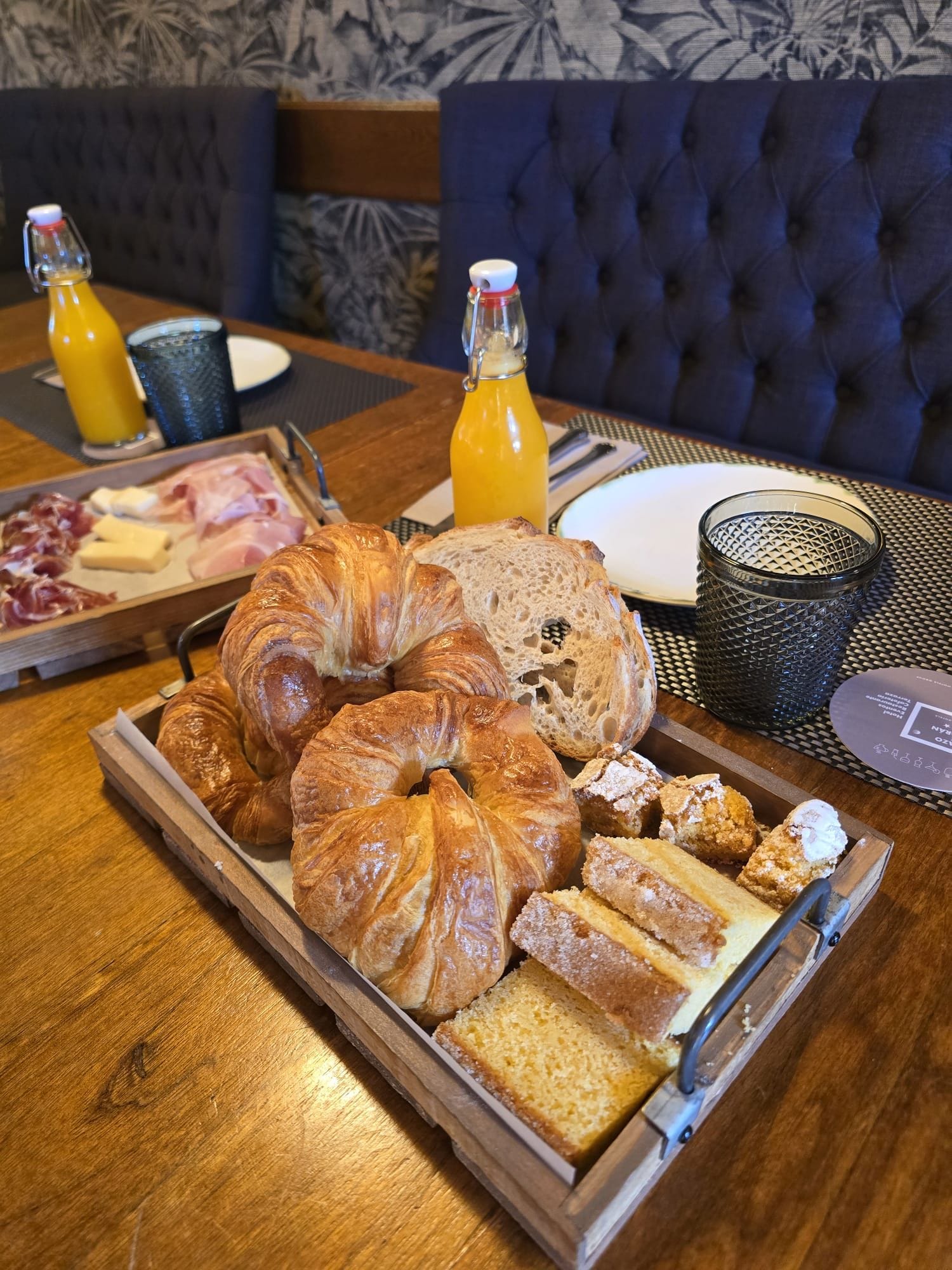 A breakfast tray with croissants, bread, pastries, and a bottle of orange juice on a wooden table.