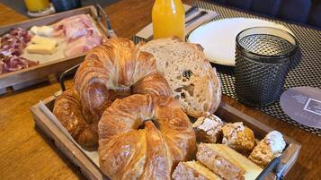 Un plateau de petit-déjeuner avec des croissants, du pain, des viennoiseries et une bouteille de jus d’orange, posé sur une table en bois.
