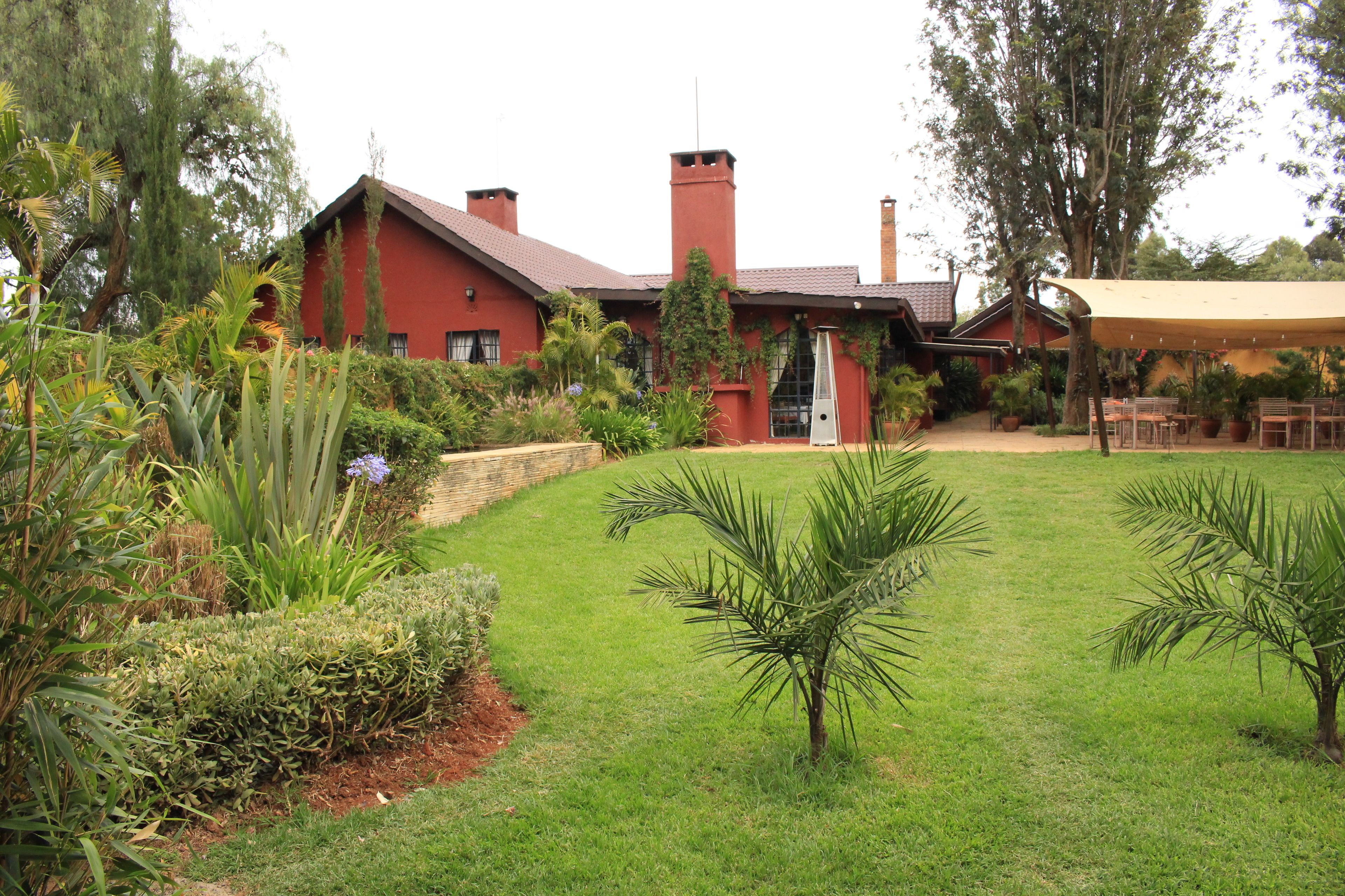 A red building with a sloped roof, surrounded by a well-maintained lawn and various plants.