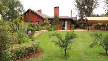 A red building with a sloped roof, surrounded by a well-maintained lawn and various plants.