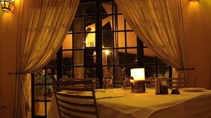 Uma sala de jantar com uma mesa posta para dois, uma vela e uma janela com cortinas.