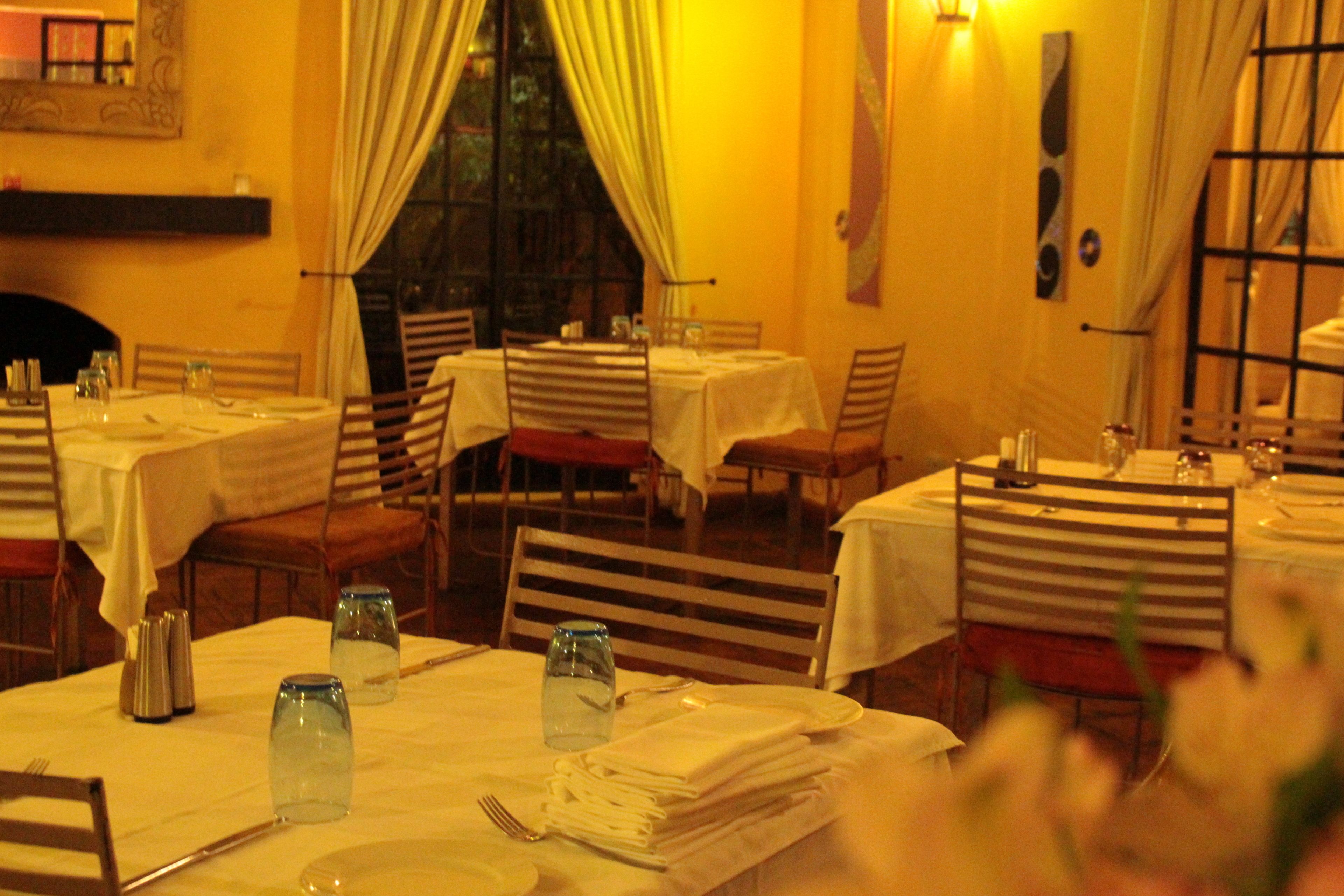 Un restaurant où de nombreuses tables sont dressées pour le service, chacune étant recouverte d’une nappe blanche et agrémentée de couverts disposés avec soin.
