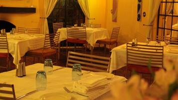 Un restaurant où de nombreuses tables sont dressées pour le service, chacune étant recouverte d’une nappe blanche et agrémentée de couverts disposés avec soin.