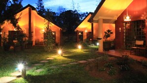 Área externa bem iluminada, com um caminho que leva a um edifício com uma janela grande e uma porta.