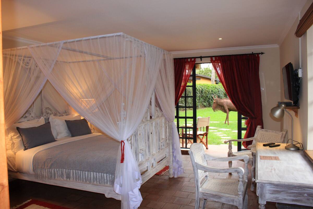 A bedroom with a four-poster bed, a desk with a chair, and a view of the garden.