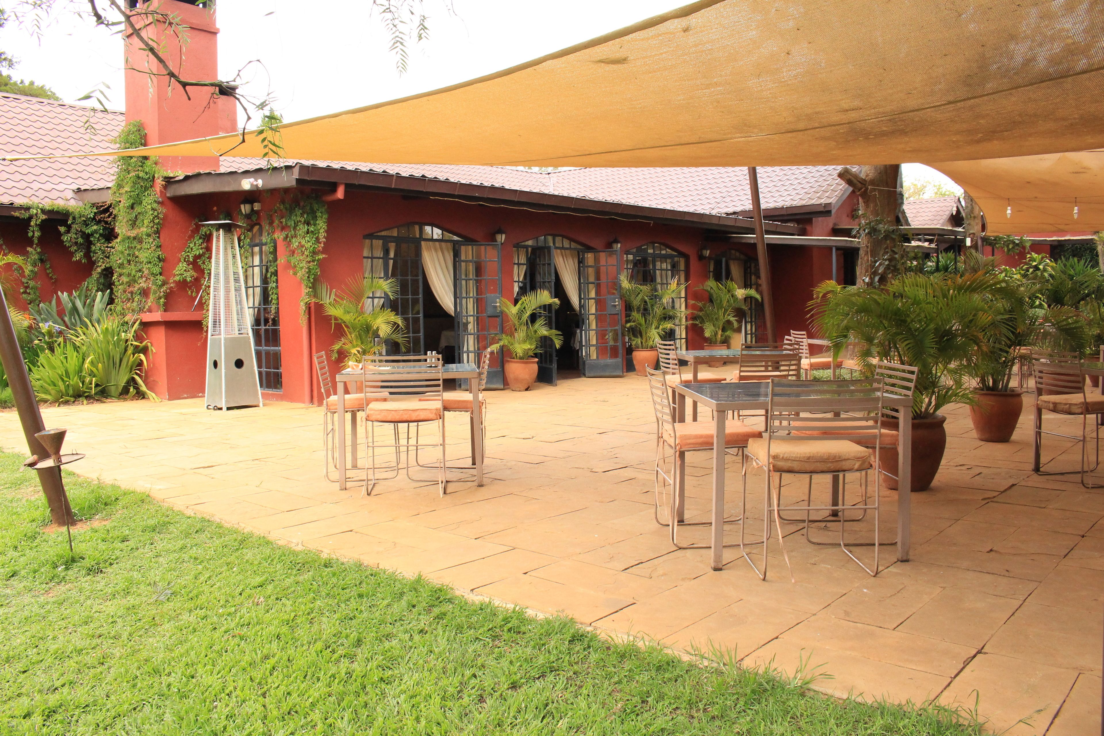 An outdoor patio area with tables and chairs, potted plants, and a building with red walls and a tiled roof.