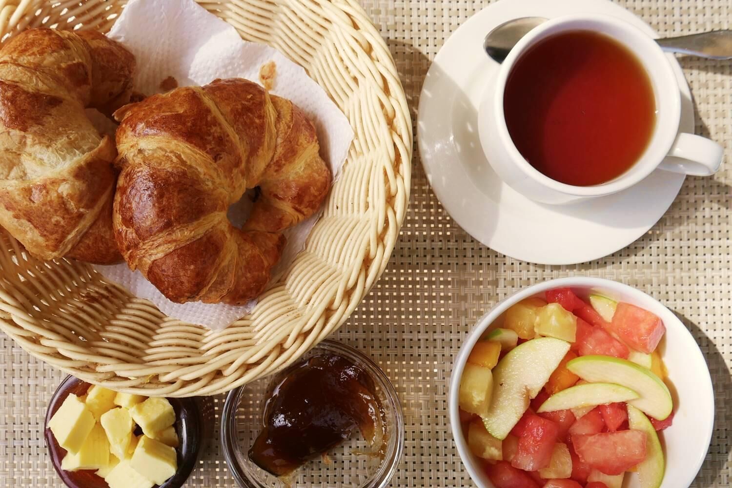 A breakfast setting with croissants, a cup of tea, and a fruit bowl.