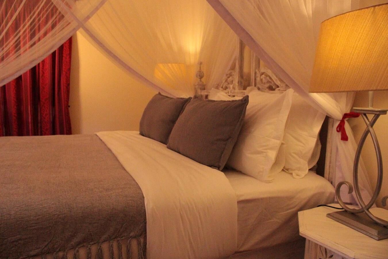 Ein Bett mit Baldachin, weißer Bettwäsche und einem roten Vorhang im Hintergrund.