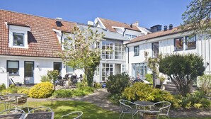 A courtyard with outdoor seating, a garden, and a row of white houses with brown tiled roofs. - Hotell Spelabäcken (Skanör)