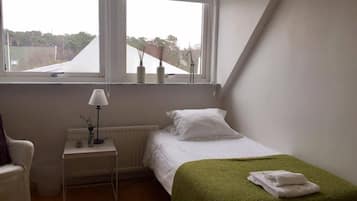 A small, tidy bedroom with a single bed, a nightstand with a lamp, and a view through a window.