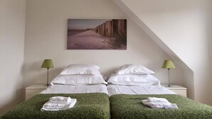 A bedroom with two beds, each with white linens and green grass-like bedding. There are two bedside lamps, a painting of a canyon on the wall, and a sloped ceiling. - Hotell Spelabäcken (Skanör)