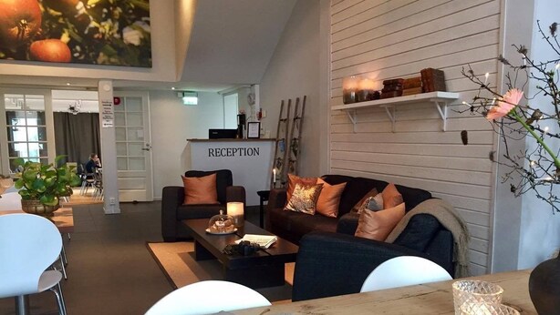 A modern reception area with a sign, a wooden reception desk, and a seating area with sofas and a coffee table. - Hotell Spelabäcken (Skanör)