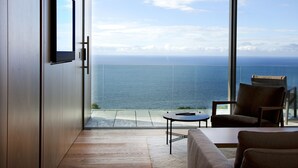 A modern room with a large window overlooking the sea, a sofa, a small table, and a chair. - Akelarre - Relais & Châteaux (San Sebastián)