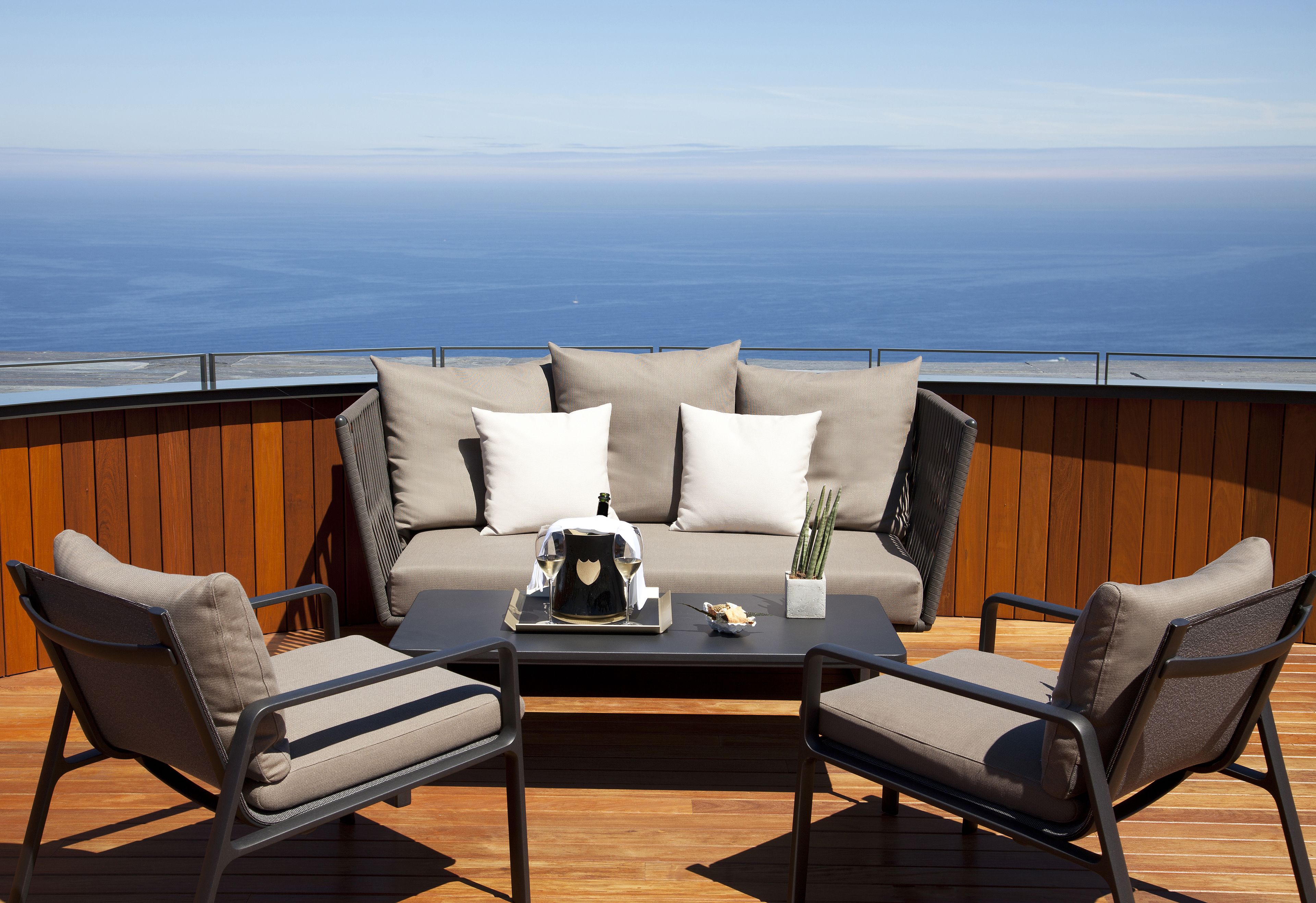 Una terraza con un sofá y dos sillones, una mesa de centro y una planta en maceta.
