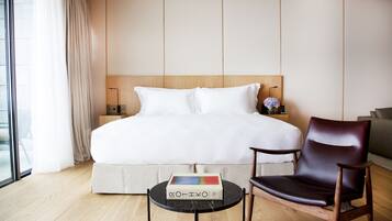 A hotel room with a large bed, a wooden headboard, a round black table with a book, a brown leather chair, and a large window with curtains.