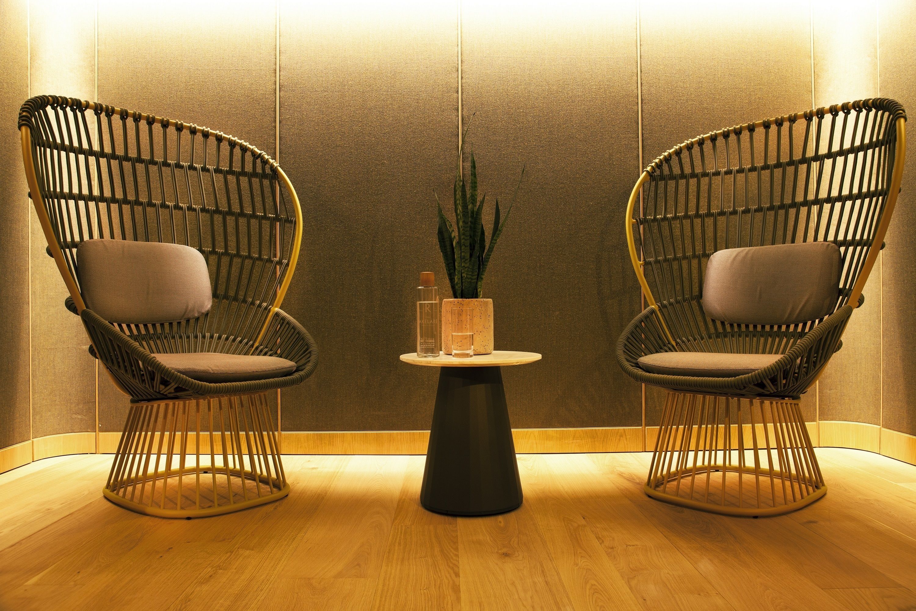 Two wicker chairs with cushions, a small round table with a plant, and a vase.