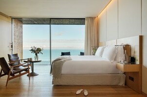 Habitación de hotel con una cama grande, una silla, una mesita y vista al océano.