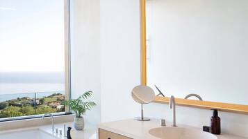 A modern bathroom with a large window, a bathtub, a sink, and a mirror.