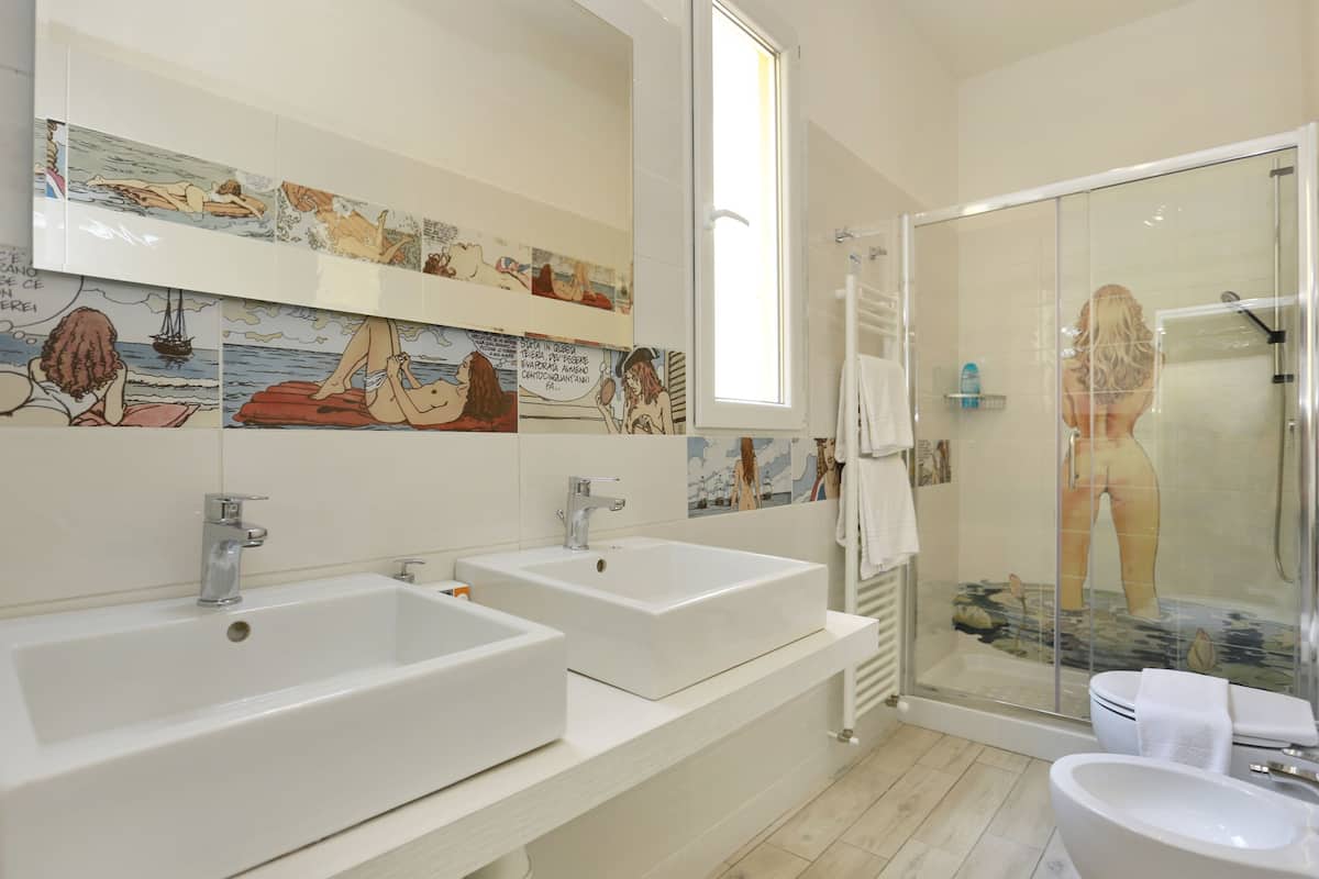 A bathroom with two sinks, a shower, and a tiled wall with a comic strip.