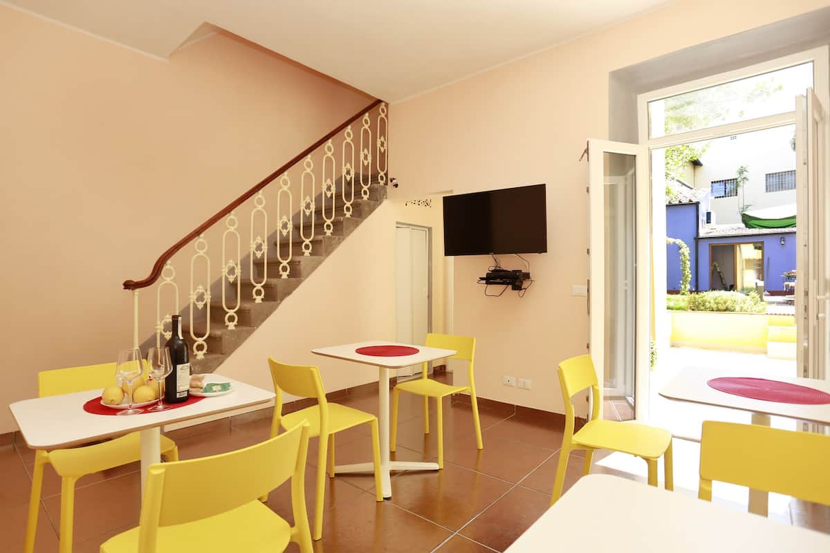 A dining area with yellow chairs and a white table, a staircase with a decorative railing, and a TV mounted on the wall.