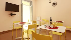 A dining area with yellow chairs and white tables, a television mounted on the wall, and a clock on the wall. - Scala Garden B&B (Florence)