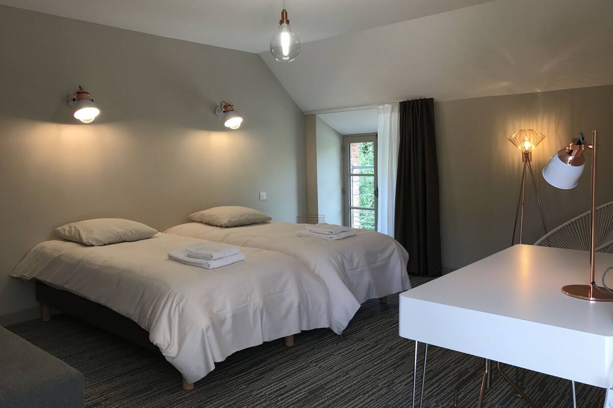 Moderni hotellihuone, jossa on suuri sänky, työpöytä ja ikkunasta avautuva näkymä vehreään maisemaan.
