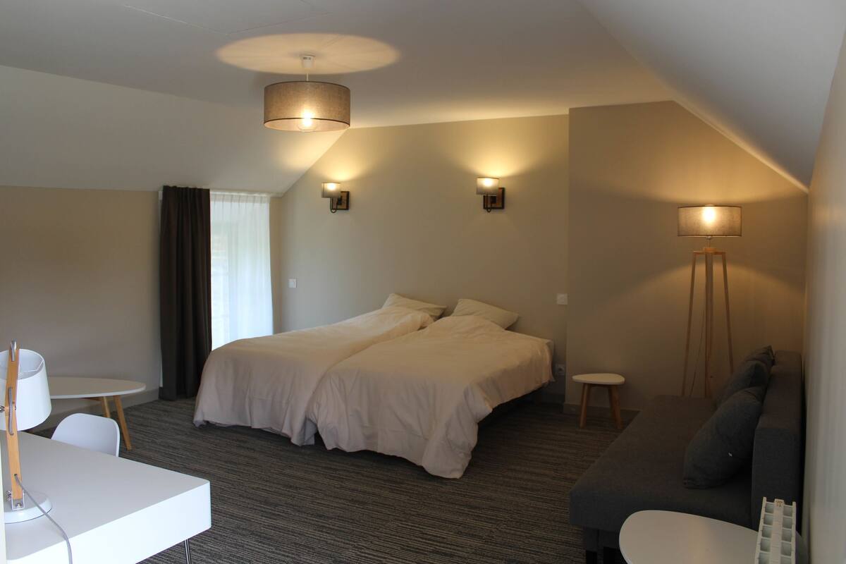 Hotellihuone, jossa on kaksi sänkyä, työpöytä, sohva ja kaksi seinään kiinnitettyä valaisinta.