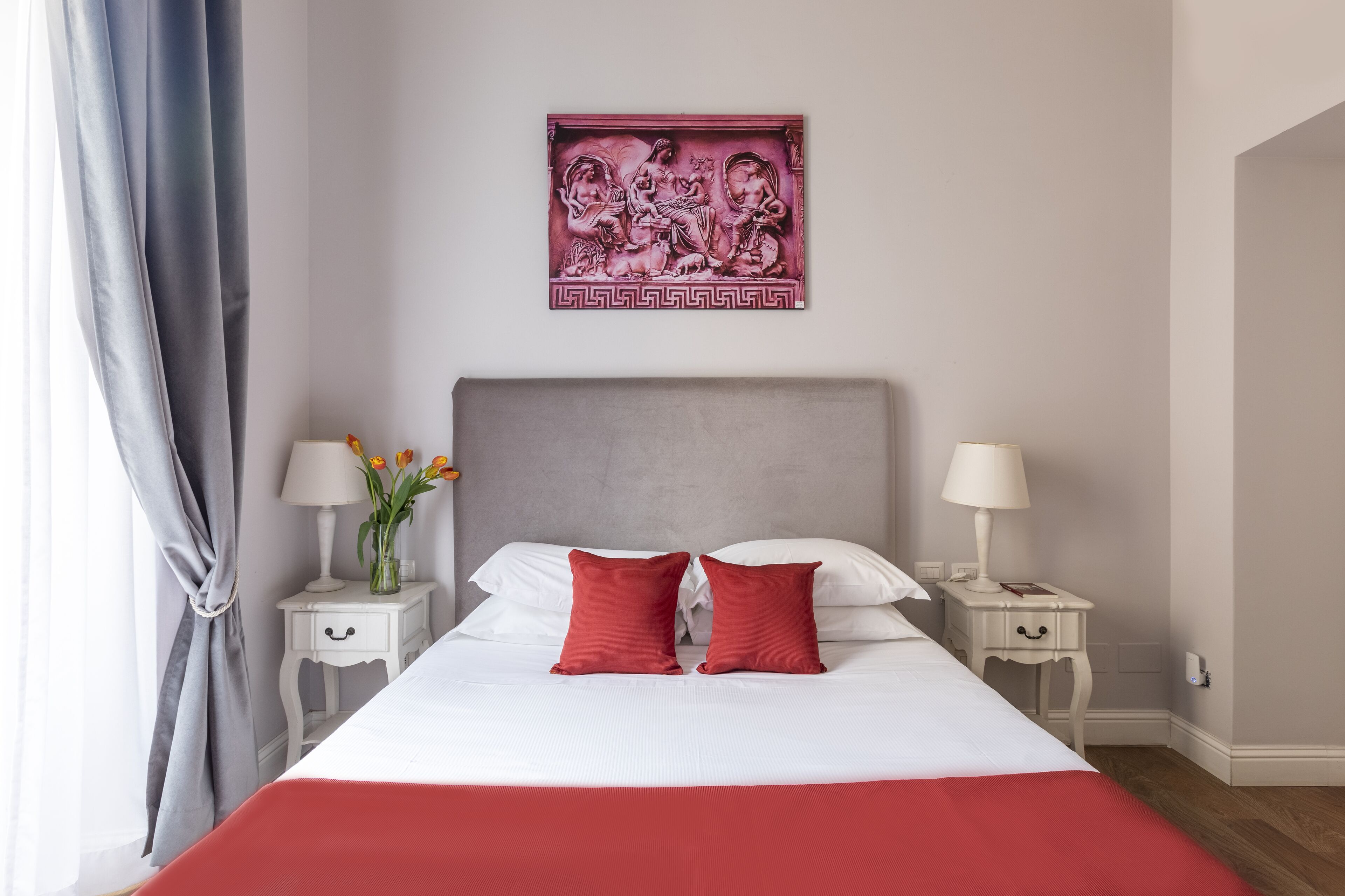 A hotel room with a large bed, two bedside tables with lamps, a decorative wall piece, and a view of the outdoors.