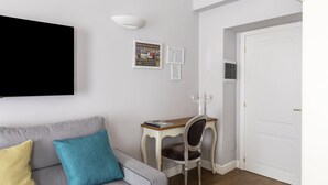A modern living room with a grey sofa, a small wooden table, and a TV mounted on the wall. - Spagna Art & Suites - Domus Collection (Rome)