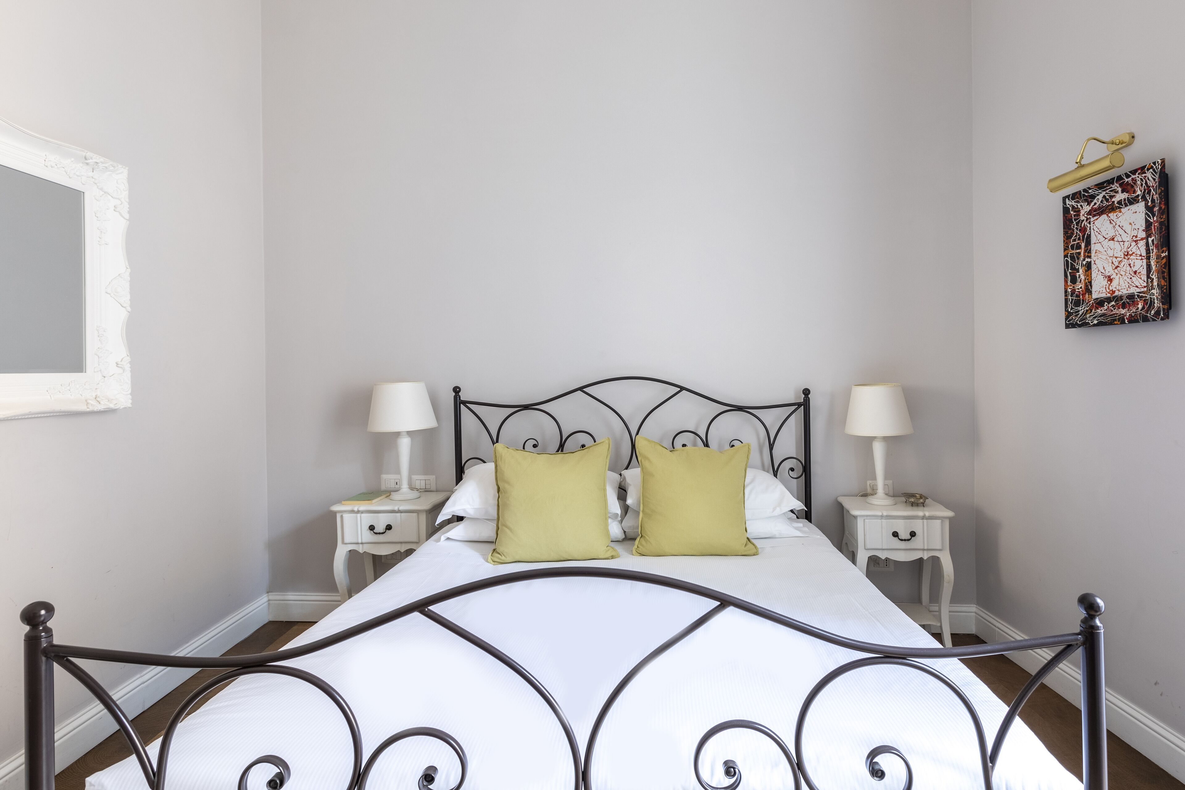 A bed with a metal frame, two bedside tables with lamps, and a wall-mounted picture frame.