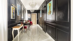 A hallway with black walls, a chandelier, framed artwork, a dining area with a table and chairs, and a door at the end. - Spagna Art & Suites - Domus Collection (Rome)