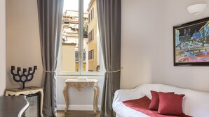 A room with a white sofa, red pillows, a menorah on a side table, and a painting on the wall. - Spagna Art & Suites - Domus Collection (Rome)
