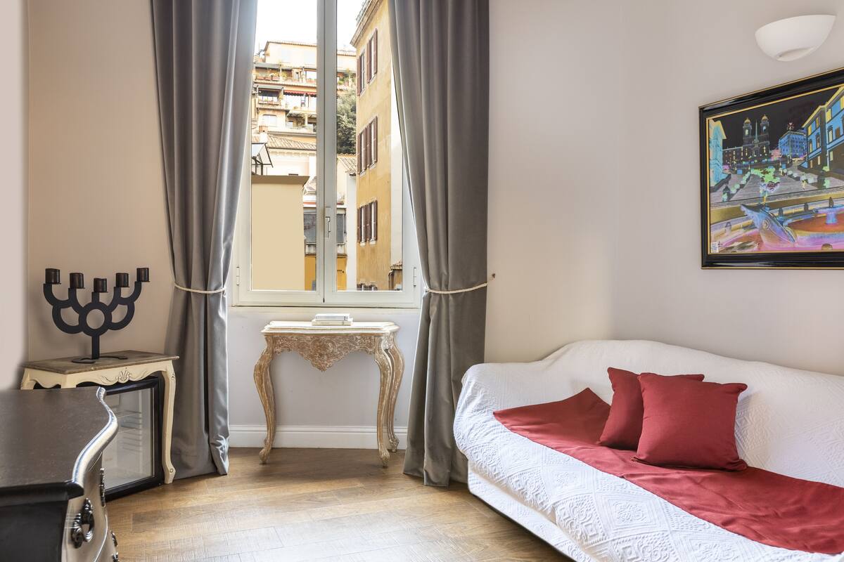 A room with a white sofa, red pillows, a menorah on a side table, and a painting on the wall.
