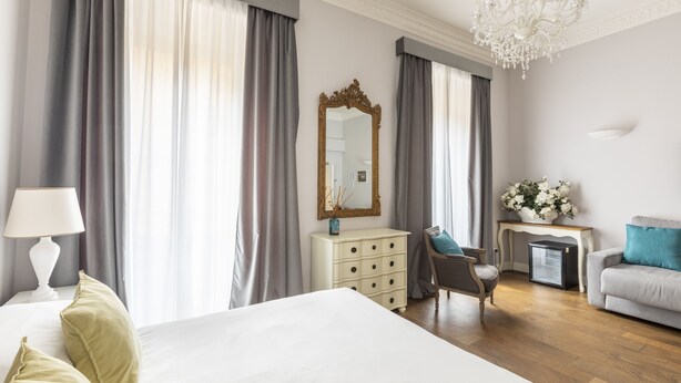 A hotel room with a large bed, a dresser, a desk, a chair, a sofa, a mirror, and a chandelier. - Spagna Art & Suites - Domus Collection (Rome)