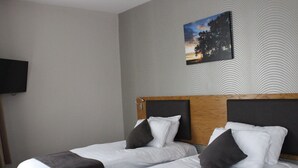 A hotel room with two beds, a flat-screen TV on the wall, and a painting of a sunset. - Ye Olde Griffin (March)
