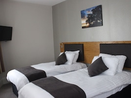 Quarto de hotel com duas camas, uma televisão de tela plana na parede e uma pintura de um pôr do sol.