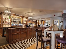 Uma área de bar com armários de madeira, piso xadrez e luminárias pendentes.
